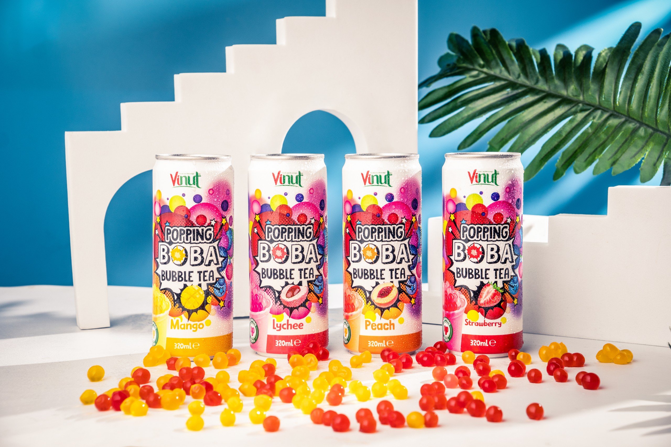 z5141685876922_3a2a2d8b33c63b86dbf742b8b6d54e58 Four cans of Vinut Popping Boba Bubble Tea in mango, lychee, peach, and strawberry flavors are displayed among colorful boba pieces on a white surface with a blue background.