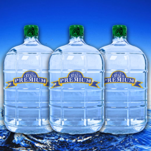 Three large clear water jugs filled with refreshing Spring Water, each with a green cap labeled "Premium," are placed side by side in front of a blue background with water at the bottom. Ideal for a 6 Bottle Plan, these 3 Gallon Glass containers ensure you always have pure hydration on hand.